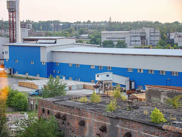Alacakaranlıktaki bir sanayi bölgesinin renkli fotoğrafında harap olmuş bir yapı ve modern endüstriyel bir bina var. Eski yapıda pas, hasar ve sebze Kostiantynivka, Ukrayna, 06-15-2013