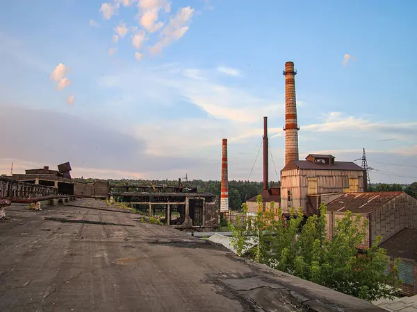 Endüstriyel bir sahne, muhtemelen şafak veya alacakaranlıkta, terk edilmiş bir binanın yakınındaki uzun bacalar, enkaz ve su birikintileriyle dolu düz olmayan toprak Kostiantynivka, Ukrayna, 06-15-2013
