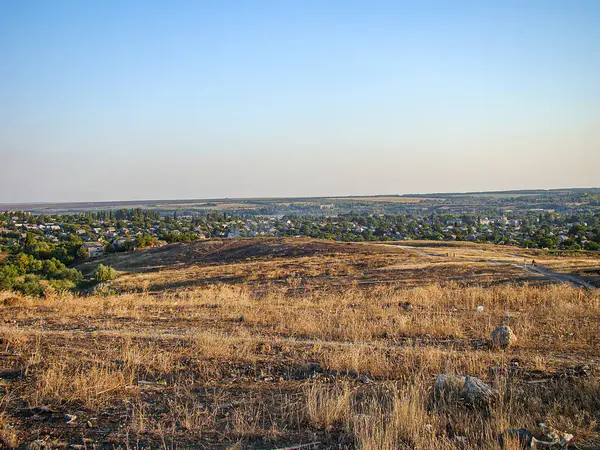 Kuru bitki örtüsü, seyrek ağaçlar, bir tepe, evler ve açık mavi gökyüzünün yer aldığı güneşli bir günün manzara görüntüsü yumuşak ışıklı, muhtemelen dur Kostiantynivka, Ukrayna, 06-15-2013