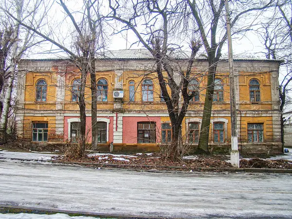 Kostiantynivka, Ukrayna, 01-15-2013 kış aylarında ya da ilkbahar başlarında karla kaplı ağaçlar ve bulutlu bir gökyüzüne kapalı pencereleri olan iki katlı renkli bir bina.