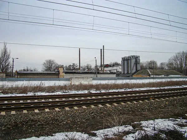 Arka planda birden fazla raylı, endüstriyel bakım yapıları olan karlı bir tren istasyonu ve durgunluk ve terk edilme hissi, Kostiantynivka, Ukrayna, 01-15-2013