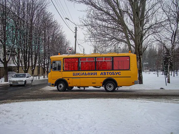 Karla kaplı ağaçların arasında buzlu bir yola park edilmiş Ukrayna metninin bulunduğu sarı bir okul otobüsü ve bulutlu bir elektrik hattı kışın ortamına hiç kimsenin Kostiantynivka, Ukrayna, 01-15-2013