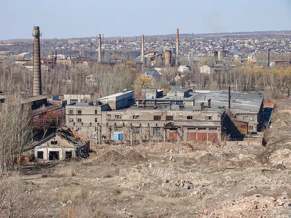 Görüntü, çürüyen binalar, düzensiz zemin ve temiz bir gökyüzü binasının altındaki uzak bacaların yer aldığı terk edilmiş bir sanayi manzarasını gösteriyor.