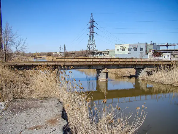 Çamurlu bir nehir üzerinde, açık gökyüzünün altında sanayi bölgesi olan işlevsel bir köprü resmi. Görünürde Kostiantynivka, Ukrayna, 06-15-2013