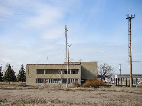 Görüntü harap olmuş bir bina gösteriyor, muhtemelen eski bir kamu tesisi veya endüstriyel bir tesis, seyrek bitki örtüsü ve Kostiantynivka, Ukrayna, 01-15-2013 sanayi bacası ile çevrili.