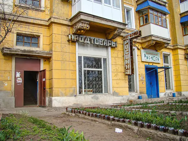 Hardal sarısı cepheli, mağaza önü ve gayri resmi bitkilere sahip eski, yıpranmış çok katlı bir bina. Dış görünüş, Cy Kostiantynivka, Ukrayna, 01-15-2013 'ten dolayı Doğu Avrupa' da olabileceğini gösteriyor.