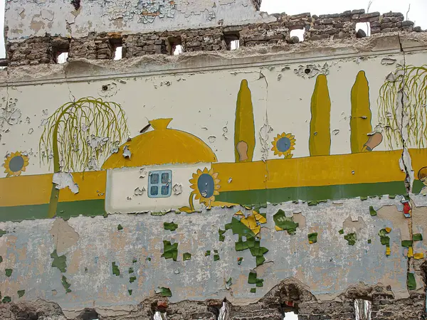 Binanın bir tarafında barışçıl bir kırsal ya da banliyö sahnesini tasvir eden yaşlanmış, hasar görmüş duvar resmi. Renkler canlı ama bakımsız Kostiantynivka, Ukrayna, 01-15-2013