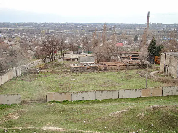 Terk edilmiş bir manzaranın seyrek bitki örtüsü, derme çatma bariyerler, hasarlı binalar, alçak duvarlar ve uzaktaki yerleşim alanları bulutlu gökyüzü, Kostiantynivka, Ukrayna, 01-15-2013