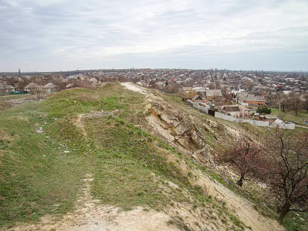 Arka planda modern kentsel binaların bulunduğu doğal bir arazide bir tepe, toprak yol ve kayaları gösteren samimi bir fotoğraf. Gökyüzü bulutu Kostiantynivka, Ukrayna, 01-15-2013