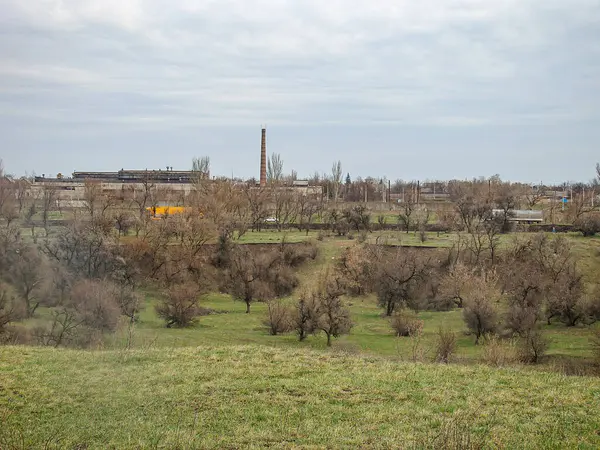 Muhtemelen sonbahar veya kış aylarında çekilen çıplak ağaçlarla kaplı açık bir arazinin siyah-beyaz manzara fotoğrafı, Kostiantynivka, Ukrayna, 01-15-2013 uzun yapıları olan bir endüstriyel kompleksi içeriyor.