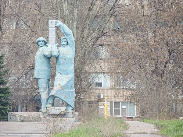 İki erkek figürden oluşan yıpranmış bronz bir heykel, biri ayakta duran ve çekiç tutan, diğeri uzanan, geleneksel kıyafetler içinde zanaatkar veya işçi olarak gözüken, si Kostiantynivka, Ukrayna, 01-15-2013