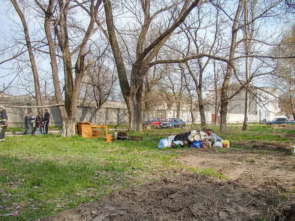 Ön planda çıplak ağaçlar, çimenler ve saçılmış yapraklarla kaplı bulutlu bir açık hava sahnesi var. Çitlere karşı ahşap bir kutunun yanında kısmen Kostiantynivka, Ukrayna, 01-15-2013
