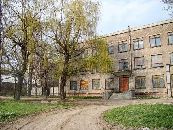 Soyulmuş boyalar, kayıp pencere camları ve çıplak ağaçlarla yaşlanmış bir şehir binası. Görüntü, sonbahar veya kış aylarında kasvetli ve sessiz bir atmosferi yakalıyor. Kostiantynivka, Ukrayna, 01-15-2013