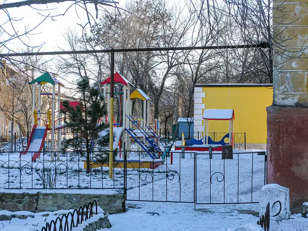 Renkli ekipmanlarla dolu bir kış gününde karlı bir oyun parkı ve arka planda sarı bir bina Kostiantynivka, Ukrayna, 01-15-2013