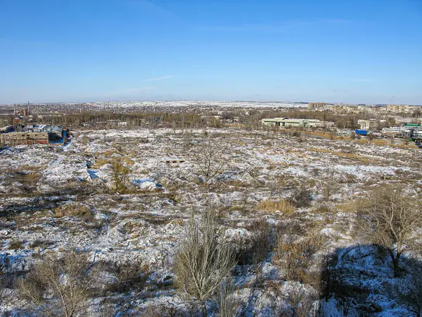 Kışın veya ilkbaharın başında dağınık ağaçlarla kaplı tepelik ve karla kaplı bir arazi, uzak endüstriyel alanlara işaret ediyor. Açık mavi gökyüzü, Kostiantynivka, Ukrayna, 01-15-2013