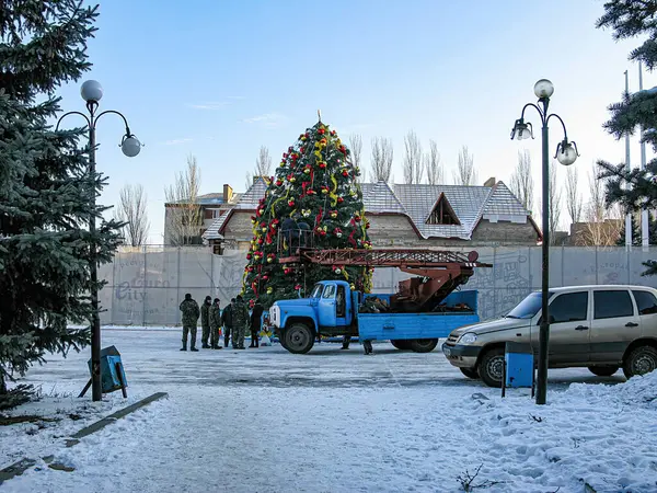 Bir grup birey dışarıda süslü bir Noel ağacı kuruyor, muhtemelen bir şehir meydanında ya da parkta, karlı zeminde bir kamyon ve araba ile Kostiantynivka, Ukrayna, 01-15-2013