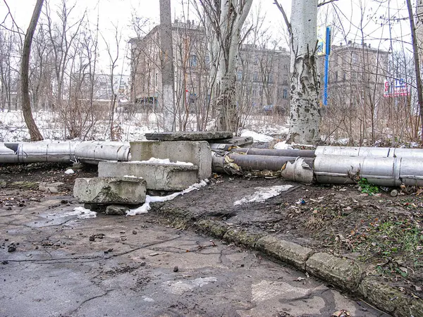 Görüntü, beton döşeme üzerinde hasarlı borular bulunan karlı bir açık hava ortamını resmediyor. Sahne, muhtemelen sonbahar veya kış aylarında Kostiantynivka, Ukrayna, 01-15-2013 'e karşı bir onarım sürecinin parçası.