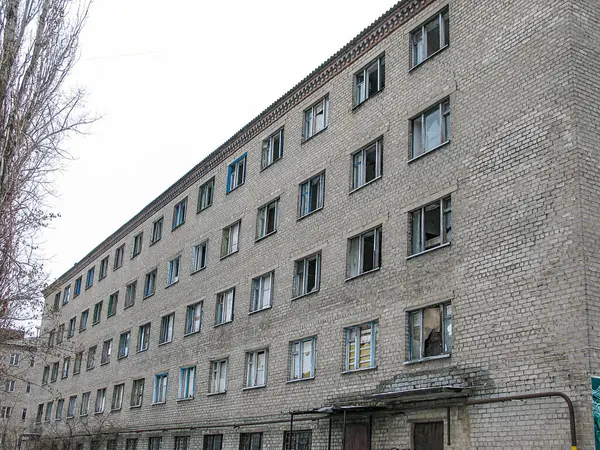 Pencereli çok katlı tuğla bir bina, bazıları kısmen kapalı ve diğerleri kısmen açık bulutlu bir günde alt pencerelerden birinde bir kişi görülüyor The Kostiantynivka, Ukrayna, 01-15-2013