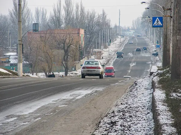 Kış ya da ilkbahar başı yol sahnesi kıvrımlı, alçalan bir yol, uzaklaşan araçlar, her iki taraftaki binalar, kar, bulutlu gökyüzü, sokak lambaları, tabelalar ve bir Kostiantynivka, Ukrayna, 01-15-2013