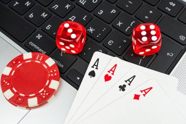 Görüntü; kumarhane eşyaları, iki kırmızı zar, poker fişi, dizüstü bilgisayardaki Ace of Mades kartları, muhtemelen kumarhane oyunları için kullanılan online kumar ya da oyun önerileri, sanal