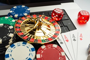 Görüntü, kumarhane temalı bir oyun düzeneği sergiliyor. Altın rulet çarkının etrafında, etrafa saçılmış fişler, kartlar ve zarlar var. Kumar aletlerine odaklanmış durumda. Risk, şans ve keyif öneriyor.