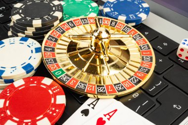 Kumar kartlarının ve geleneksel kumarhane ve online oyun oyunlarının bir klavye karışımının olduğu oyun ortamında, numaralandırılmış slot makineleri olan altın rulet tekerleğinin yakın plan görüntüsü.