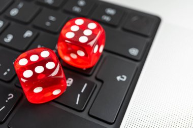 Görüntü, siyah bir klavyede beyaz harfli iki kırmızı zar tasvir ediyor. Muhtemelen oyun ya da kumar bağlamında fiziksel ve sanal dünyaların harmanlandığını gösteriyor.