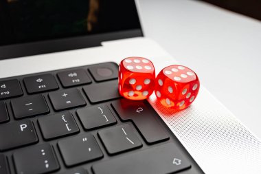 Açık bir dizüstü bilgisayarda iki renkli zar resmi, kısmen görünür klavye, karanlık bir görüntü gösteren dizüstü bilgisayar, oyun ve teknoloji bağlantısını vurguluyor