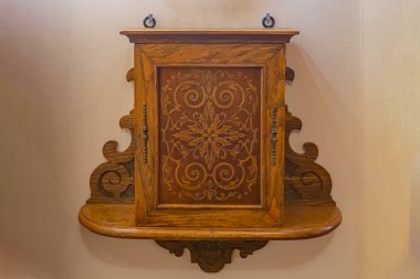 Karmaşık oymalarla bej duvara monte edilmiş, süslü ahşap bir dolap ve kemerli bir üst tasarım, antika estetiğini geliştiren merkezi bir dekoratif panel içeriyor.