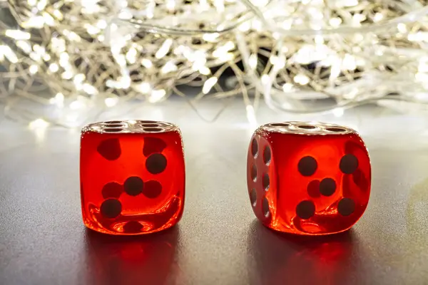 Siyah noktalı iki kırmızı cam zar, gece karanlığında bulanık bir zemin üzerine yerleştirilmiş, muhtemelen Noel gibi bir şenlik, sicim ışıkları ve oyun için uygun sıcak bir parıltı,