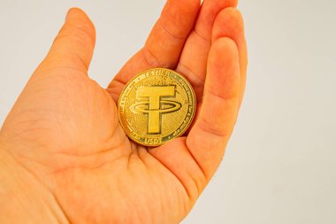 Bir el, nötr bir arkaplana karşı, kripto para bağının elle tutulur temsilini vurgulayan ayrıntılı bir para sikkesi tutar.