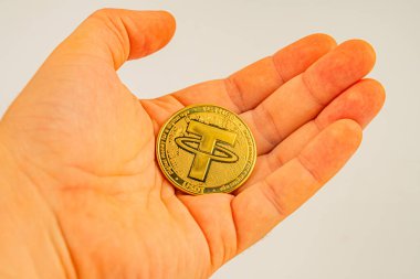 Üzerinde Bitcoin logosu olan altın testereli bir madeni parayı tutan bir elin yakın plan görüntüsü.