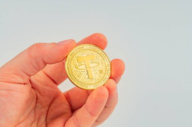 Görüntü, karmaşık tasarımları olan, zenginliği, yeniliği ya da dijital para birimlerine yapılan yatırımı sembolize eden, altın bir halat sikkeyi tutan bir eli gösteriyor.