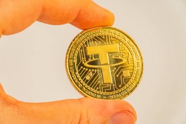 Bir reklam resmi bulanık arkaplana karşı bir el tarafından tutulan bir bozuk para jetonunu gösterir. Jeton somut değeri ya da şifrelenebilir para bağını sembolize eder.