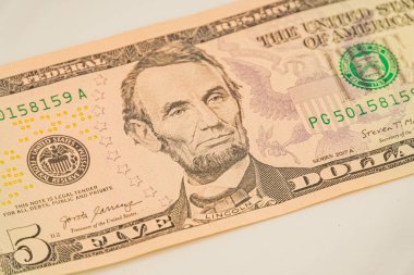Abraham Lincoln profilli ve filigran 5, ABD 'li beş dolarlık bir banknotun resmi. Yasa bir yüzeye yerleştirilmiş, ancak ayarı ya da durumu bu açıdan belirsiz.
