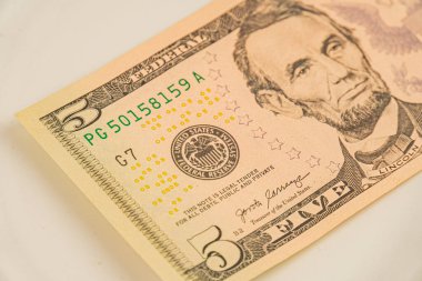 Abraham Lincoln 'ün, finans veya ekonomi tartışmalarında kullanılan belirgin filigran ve seri numaraları bulunan beş dolarlık yakın plan Amerikan banknotunun görüntüsü.
