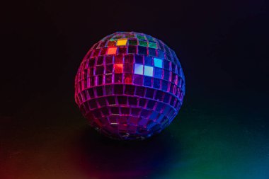 Disko topu çok renkli ışıklarla karanlık bir arkaplanda, canlı renkleri yansıtıyor disko dönemi atmosferini yakalıyor