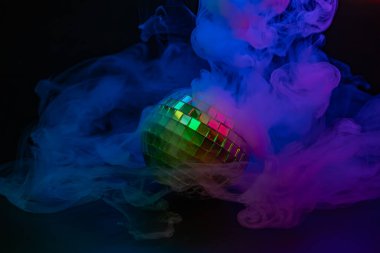 Karanlık bir arka planda kıvrımlı renkli dumanı olan hareketli disko topu imajı, genellikle partiyi, kutlamayı veya eğlenceyi sembolize etmek için kullanılır.