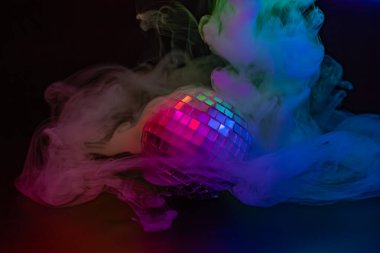 Karanlık bir ortamda renkli ışık saçan bir disko topunun görüntüsü, sis veya dumana benzer bir etki yaratarak eğlence ve kutlama iletir