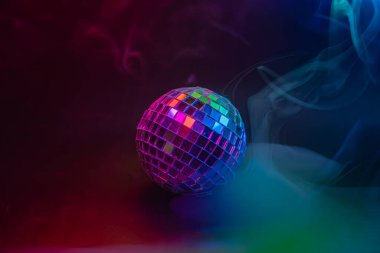 Renkli, dinamik bir arka planı olan canlı bir disko topunun görüntüsü, 1970 'lerin disko dönemiyle ilgili partilerin ve kutlamaların temaları olan ışığı yansıtıyor.