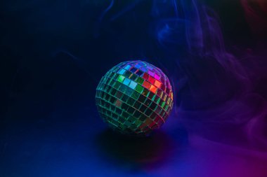 Karanlık yüzeyde disko topu, renkli ışıkları ve bir partiye veya şenlikli bir arka plana karşı hafif duman efektlerini yansıtıyor