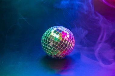 Canlı bir disko görüntüsü renkli, köpüklü efektler ve dumanlı atmosfer arasında bir disko topu sergiliyor. Eğlenceyi, kutlamaları ve gece enerjisini simgeliyor.