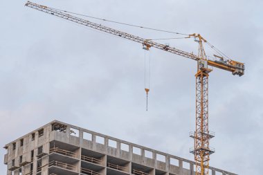 Bir inşaat fotoğrafında birden fazla katlı, görünür beton kirişleri ve kolonları olan bir bina var. Ağır kaldırma faaliyetleri için uzun sarı bir vinç var.