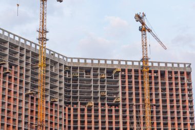 Yüksek çözünürlüklü bir inşaat alanı görüntüsü. Birden fazla bina geliştirme aşamasında. Sarı vinçler iş başında ve parçalı bulutlu gökyüzü.