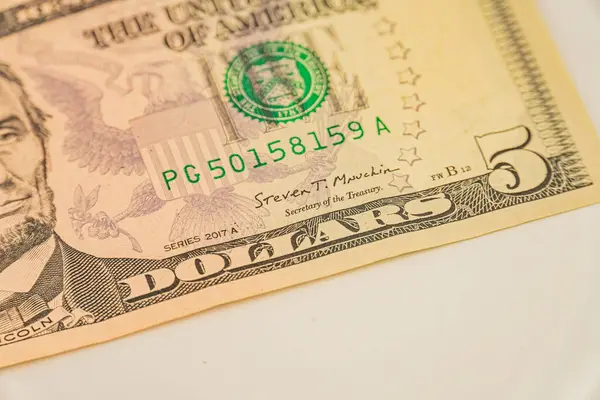 Bir görüntüde, maliye ve ekonomik tartışmalarda veya tarihsel tartışmalarda kalpazanlığı önlemek için güvenlik unsurlarının yer aldığı, Başkan Abraham Lincoln 'un portresi ile bulanık bir ABD 5 dolarlık banknot yer alıyor.