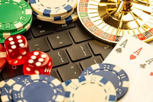 Görüntü dizüstü bilgisayarın kenarındaki kumar eşyalarının bir koleksiyonunu gösteriyor, oyun kartları, kumarhane fişleri, rulet çarkı ve zar gibi online oyun ve kumarhane uygulamalarını öneriyor.