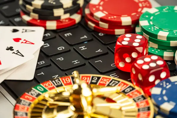 Görüntü, kart, fiş, zar oynayan kumarhane eşyalarının bir dizüstü bilgisayarın arka planında dağıldığını gösteriyor. Çevrimiçi oyun ya da teknoloji tabanlı kumarhane teması öneriliyor.