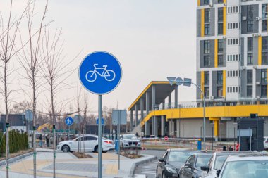 Görüntü, bisiklet yolu, modern mimari, park edilmiş araçlar ve açık gökyüzü altında yayalar olan bir şehir manzarasını gösteriyor: Kyiv, Ukrayna, 09-15-2024