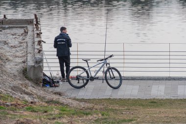 Üniformalı bir kişi, sakin bir su kütlesinin yanında balık tutuyor. Bu da çevre dostu ulaşım bisikleti Kyiv, Ukrayna, 09-15-2024 ile açık hava eğlencesi olduğunu gösteriyor.