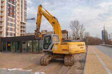 Ön planda aktif sarı bir kazıcı ve arka planda yapım aşamasında olan çok katlı bir inşaat sahası Kyiv, Ukrayna, 09-15-2024